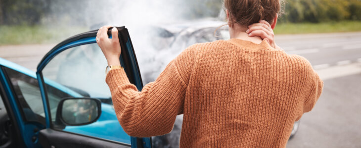 Rear View Of Female Motorist With Head Injury Getting Out Of Car After Crash