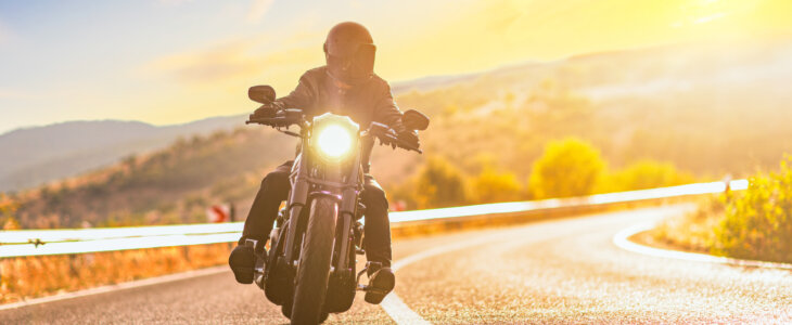 Sunset over an open road and a man with a helmet riding a chopper motorbike