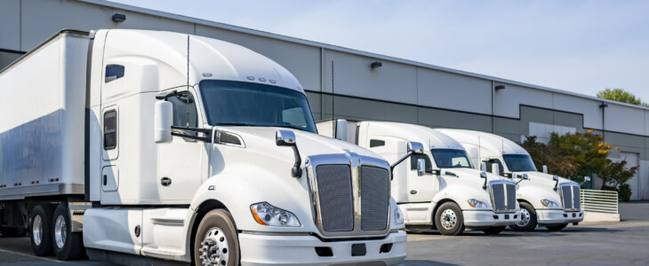 Industrial long hauler carriers white big rig semi trucks tractors with high cab for truck driver rest standing on the parking lot in warehouse docks gates loading cargo for the next delivery freight