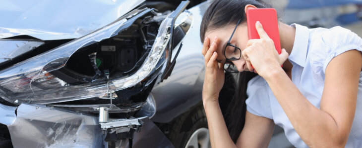 Sad woman talking on cell phone near wrecked car. Female driver concept