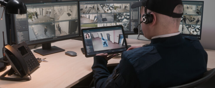 Security officer in headset controls and monitors CCTV cameras in coworking office, uses digital tablet and computers with playback on screens. High tech software showing surveillance cameras footage.