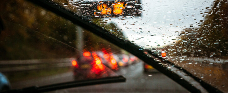 Wipers clearing rain, and roads busy with traffic as the light fades on a winter commute.