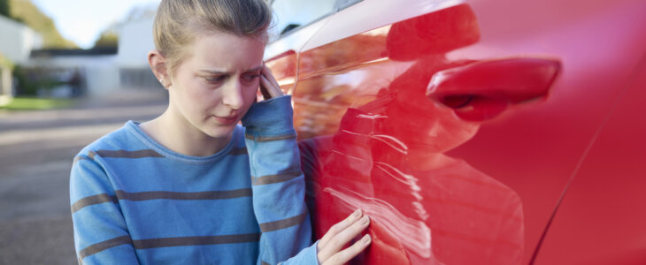 Young Worried Teenage Female Driver Looking At Damaged Car After Accident