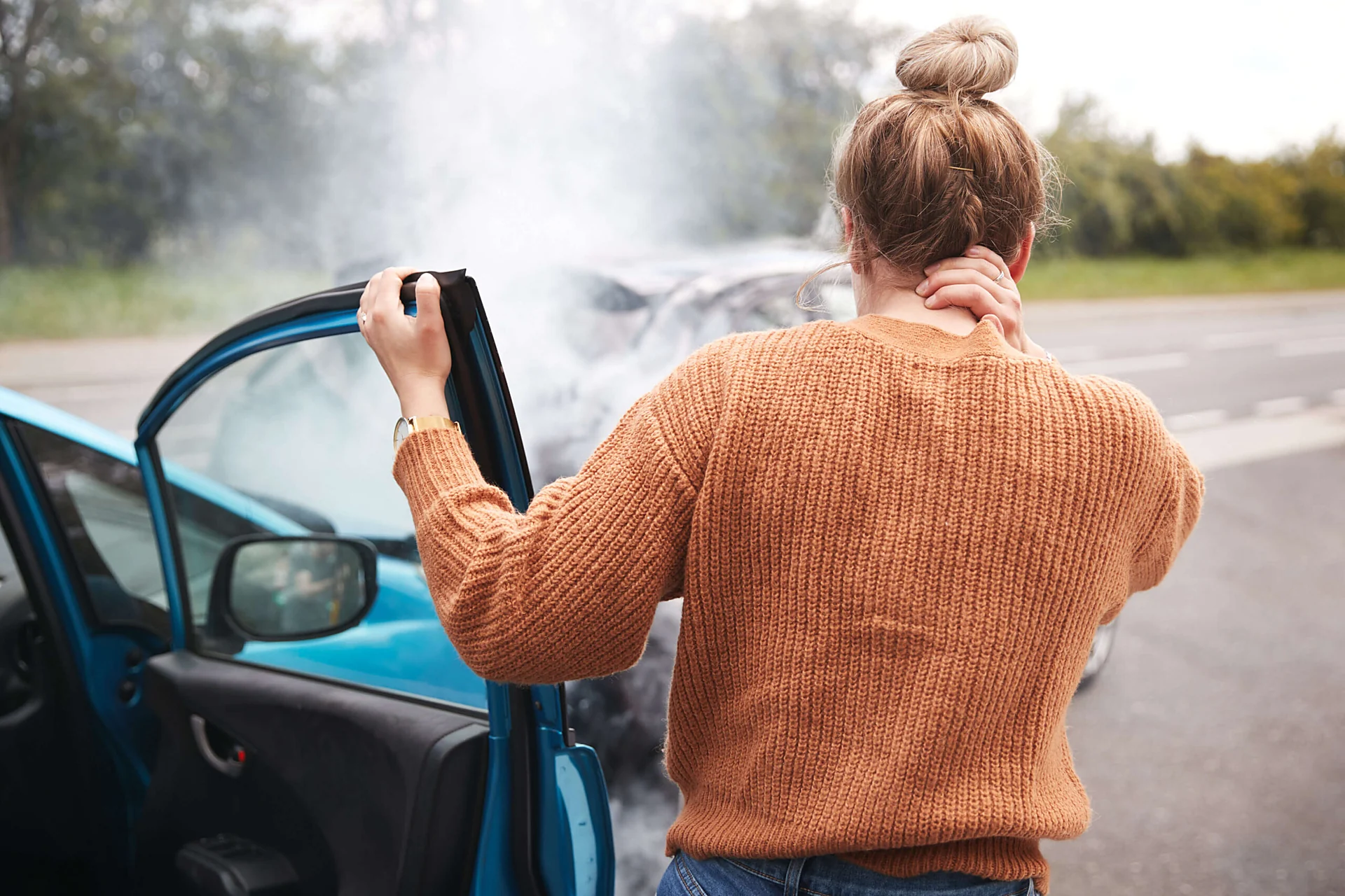 Gastonia car accident lawyer for a driver holding her neck beside a smoking car